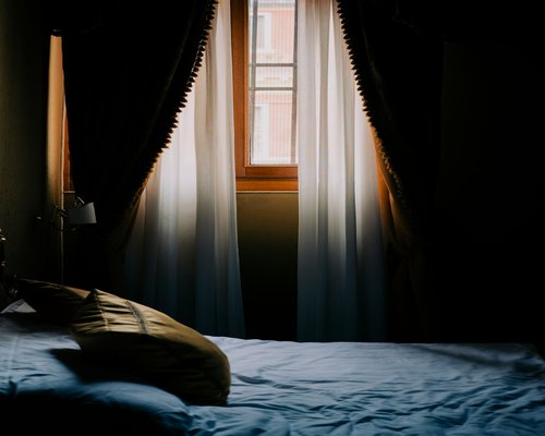 Comfortable tidy bed in a room with warm morning light filtering through curtains