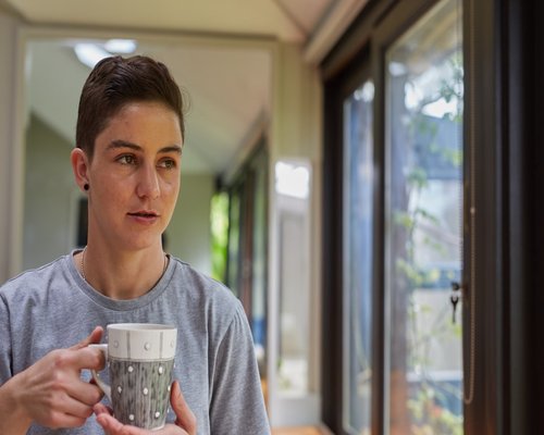 Person holding a warm mug looking thoughtfully out the window
